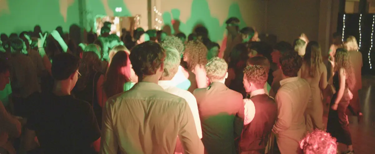 Foule d'élèves de dos sur la piste de danse d'un bal de promo, sous les lumières vertes et rouges — captation vidéo d'événements lycéens