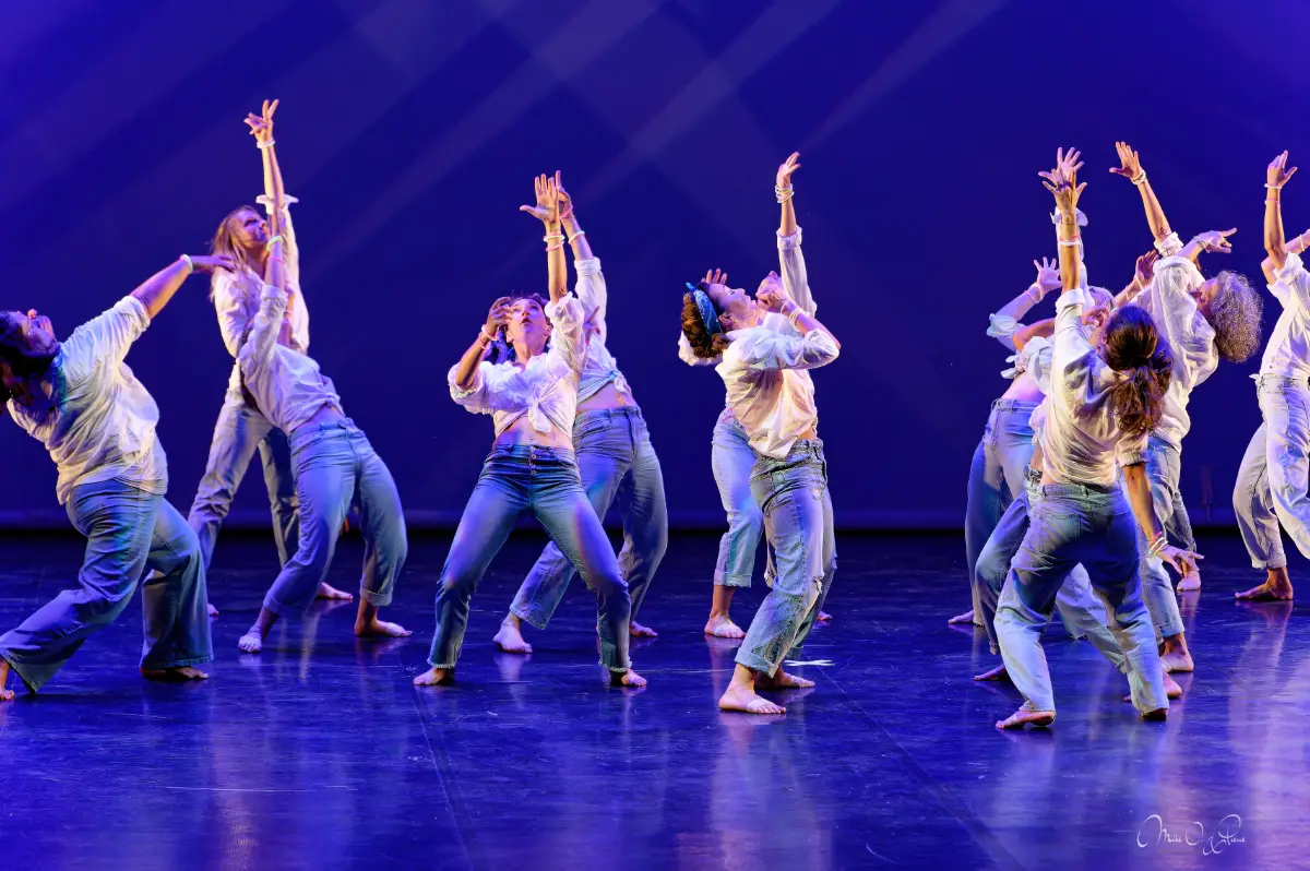 Danseuses en chemises blanches et jeans sur scène lors du gala de Ka'Danse à Arcachon, lumière bleue de spectacle, bras levés